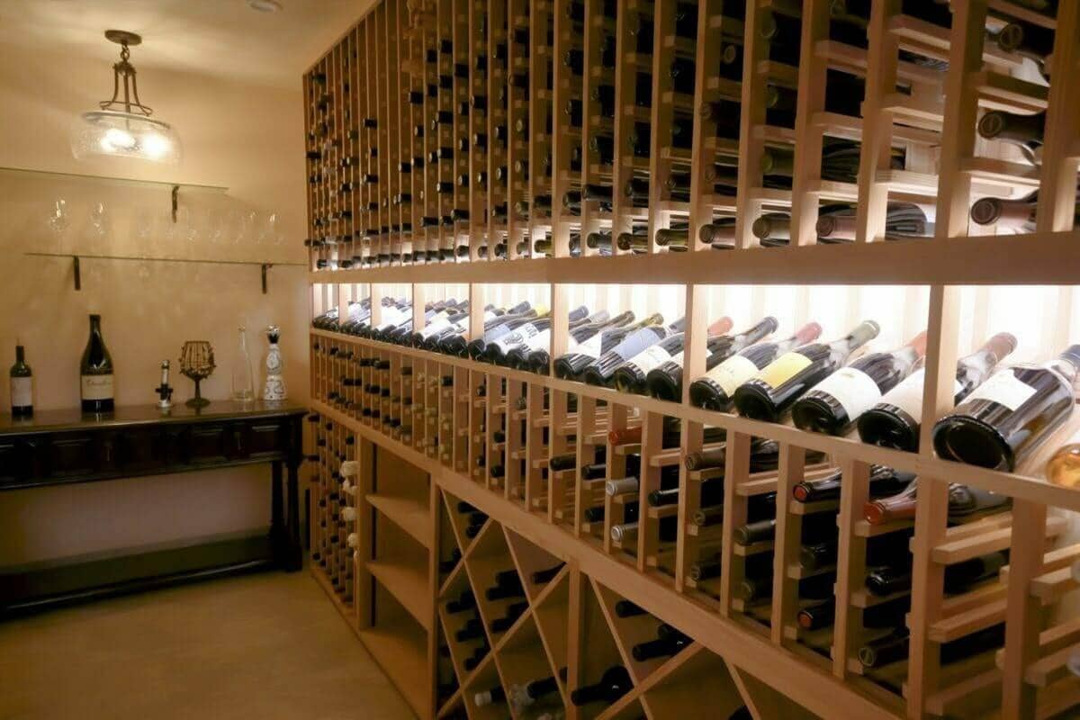A long wooden rack wall with a lit display row stands beside a cellar bar.