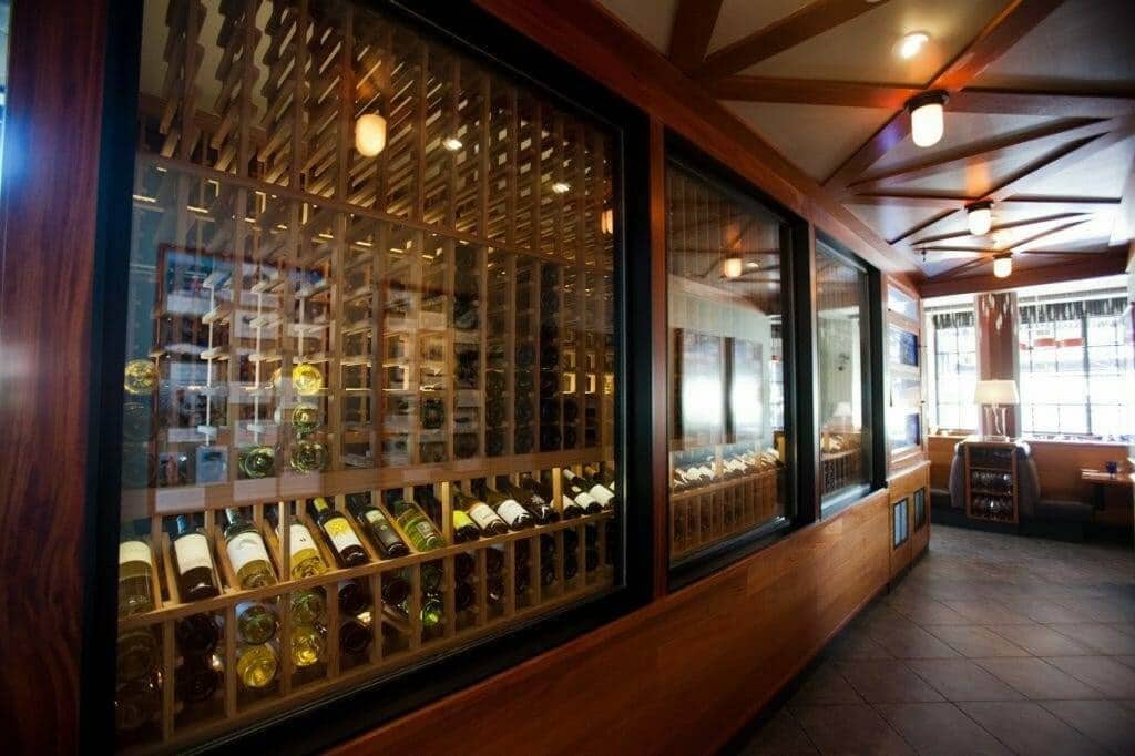 Glass-front wine storage with wooden racks lines a restaurant corridor.