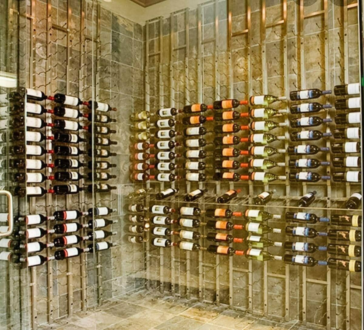 Metal bottle cradles hold wine against a textured stone wall behind glass.