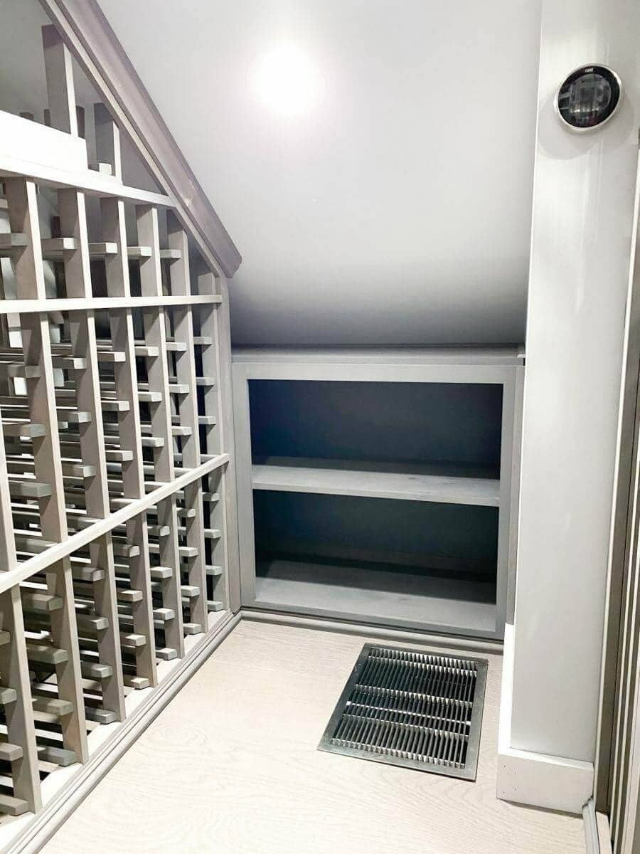 Gray bottle racks and open shelves fit beneath a sloped ceiling beside a floor grille.