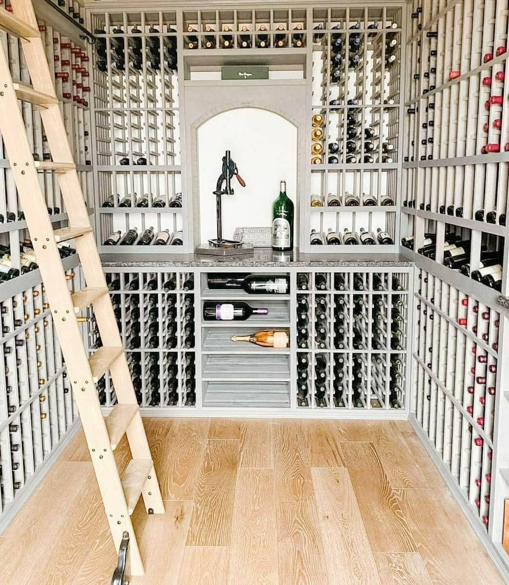 A wooden ladder stands beside gray bottle racks and an illuminated central display alcove.