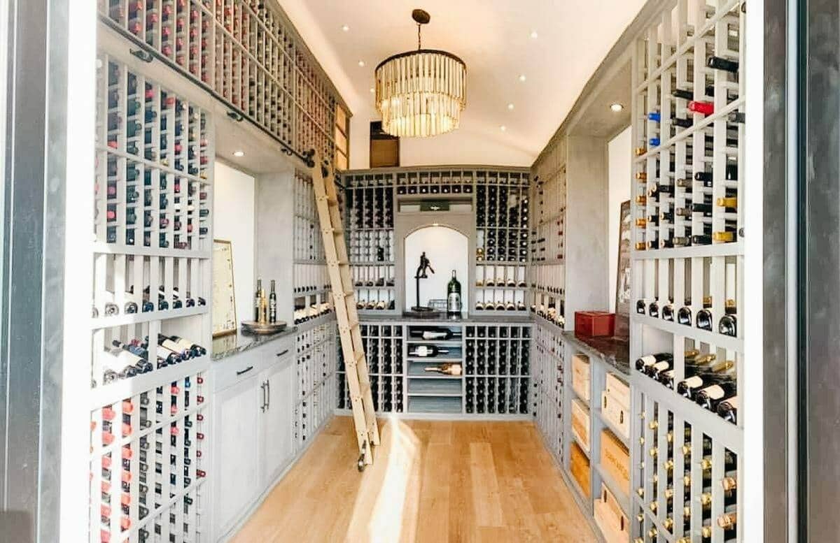 A central aisle leads through gray cellar racks past a wooden ladder and display counters.
