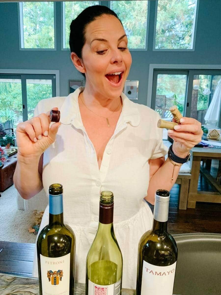 Woman laughing while holding a cork and screwcap over three wine bottles