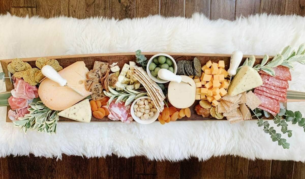 Long charcuterie board with meats, cheese and crackers on a white fur rug