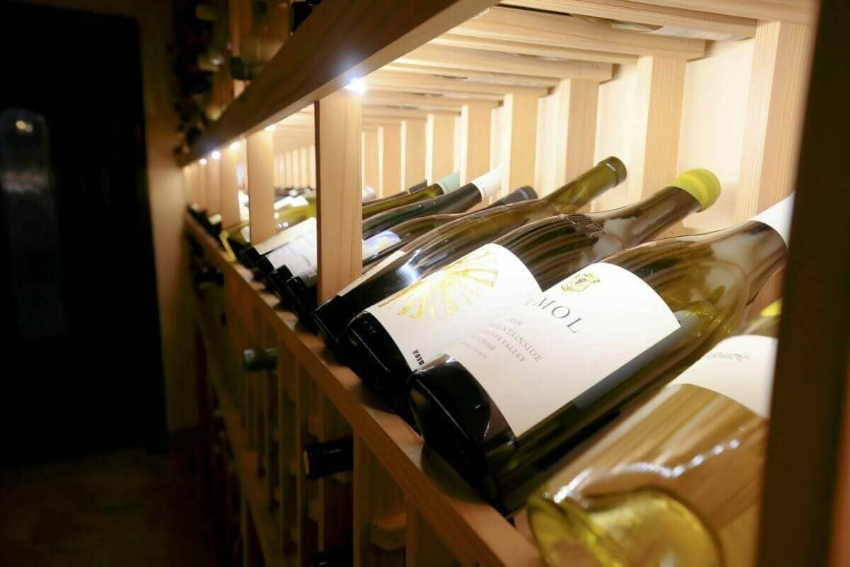 Close-up of white wine bottles resting on a lit wooden cellar rack.