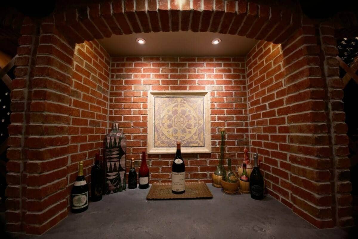 Bottles and framed artwork fill a warmly lit brick cellar alcove.
