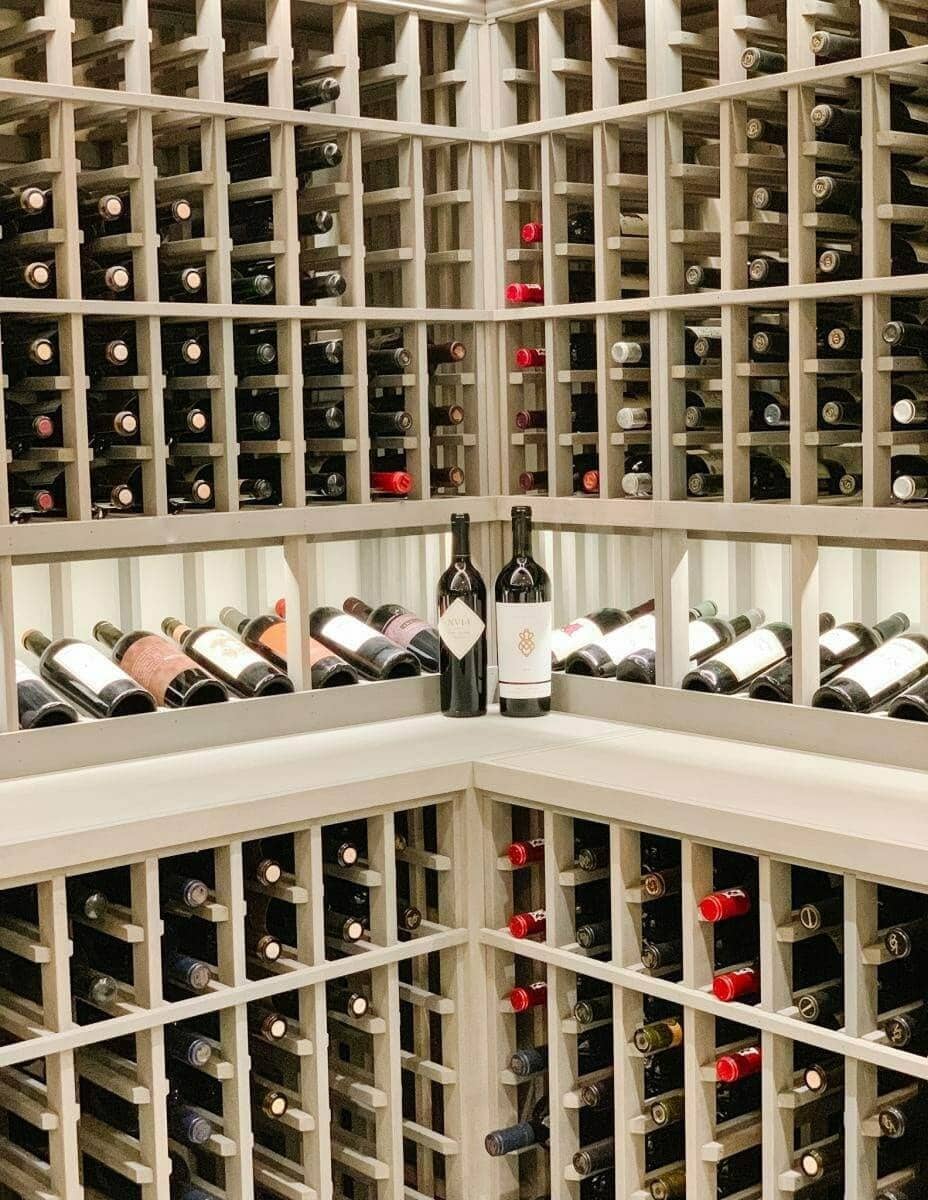 Gray wooden racks meet at a corner with an illuminated bottle display row.