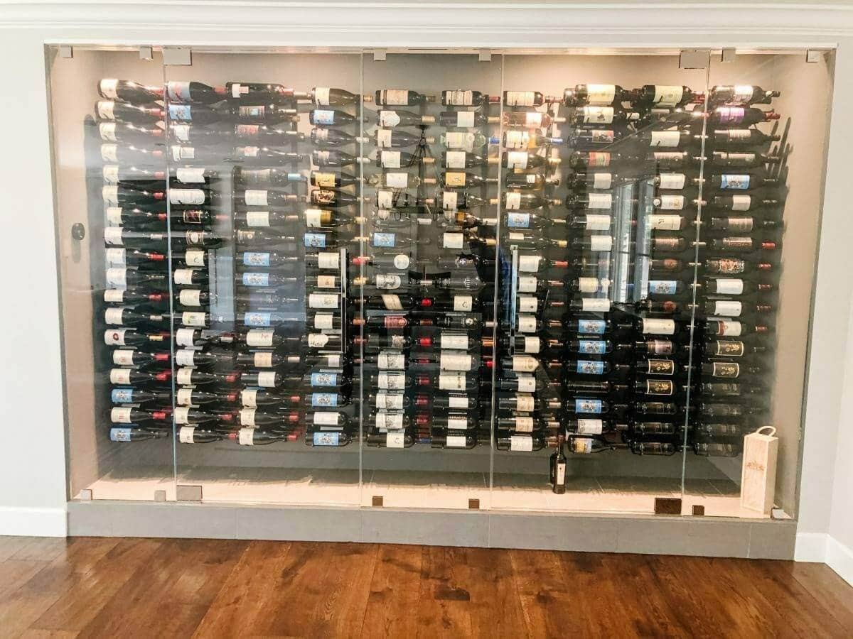 A wide glass-front wine wall displays bottles on horizontal metal racks.