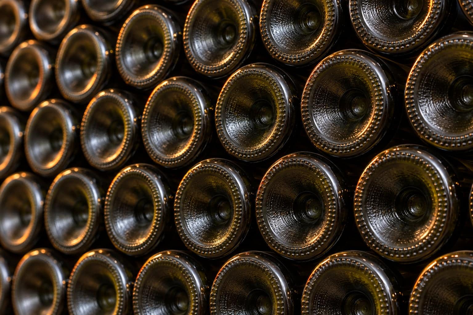 Macro shot of champagne-style punted bottle bases stacked in angled cellar rows