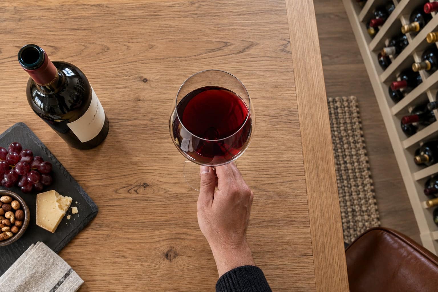 A hand holding a glass of red wine above a wooden tasting table
