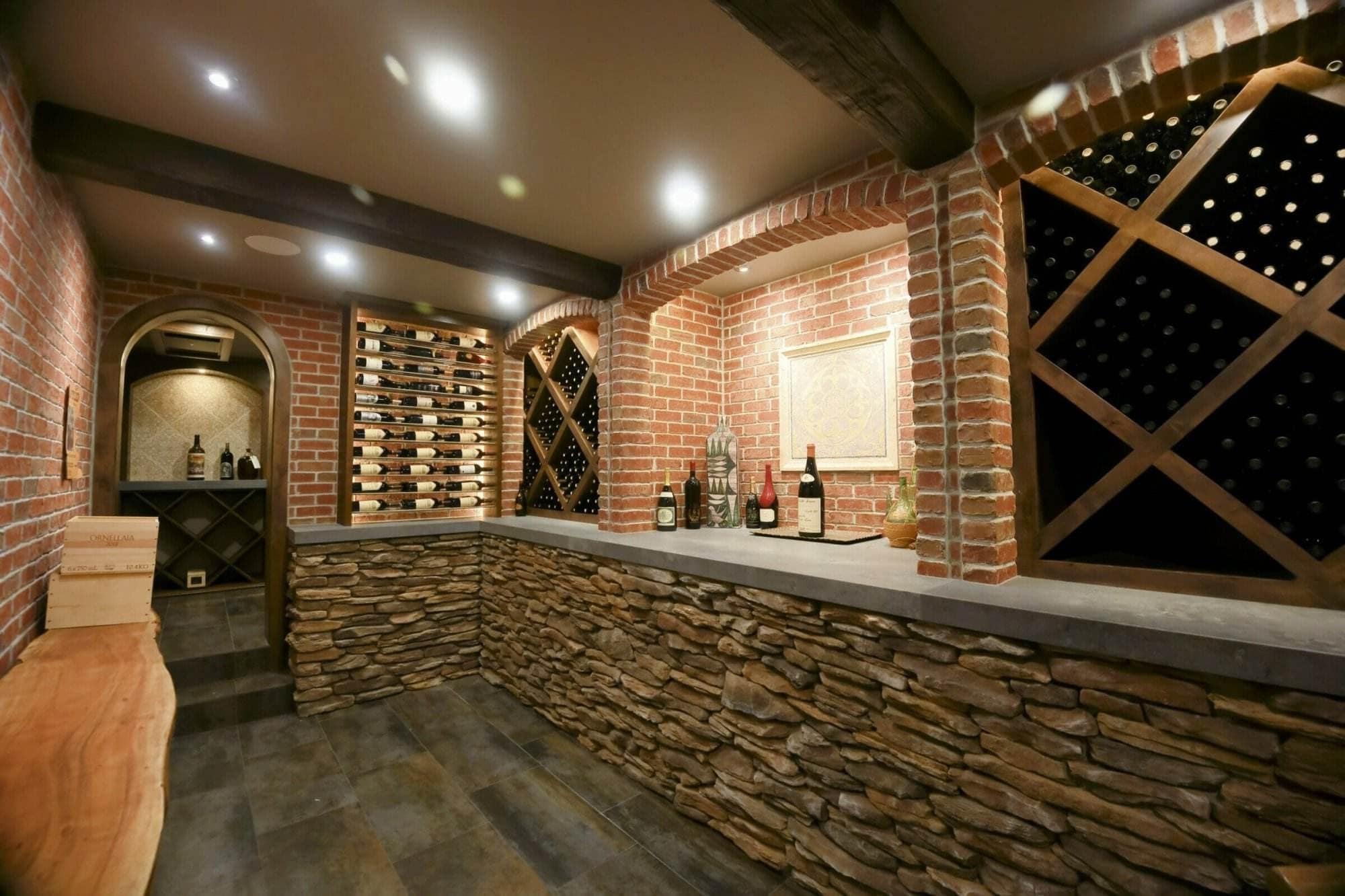 A brick arch frames a cellar bar between label-forward racks and wooden diamond bins.