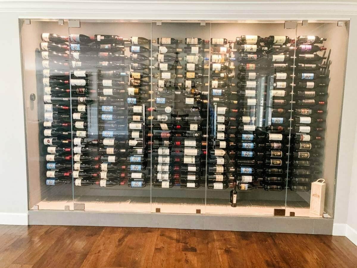 A wide glass-front wine wall displays bottles on horizontal metal racks.
