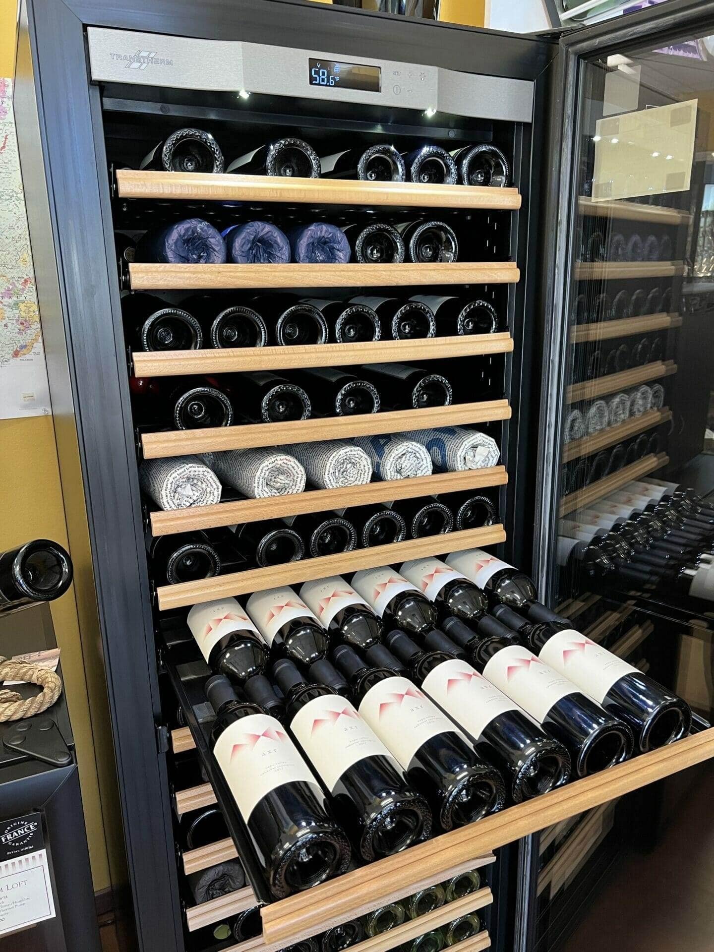 Transtherm wine cabinet drawer of red wine bottles beneath rolled towels and shelves