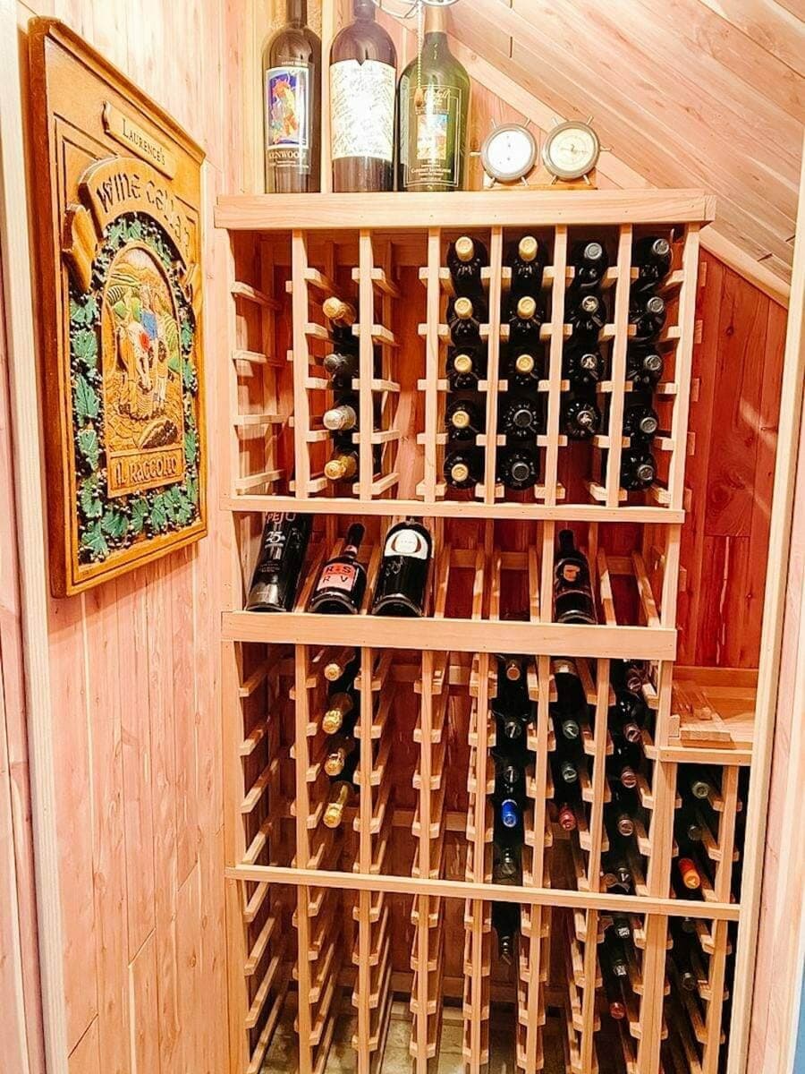 Wooden bottle racks follow a sloped ceiling beside a framed wine poster.