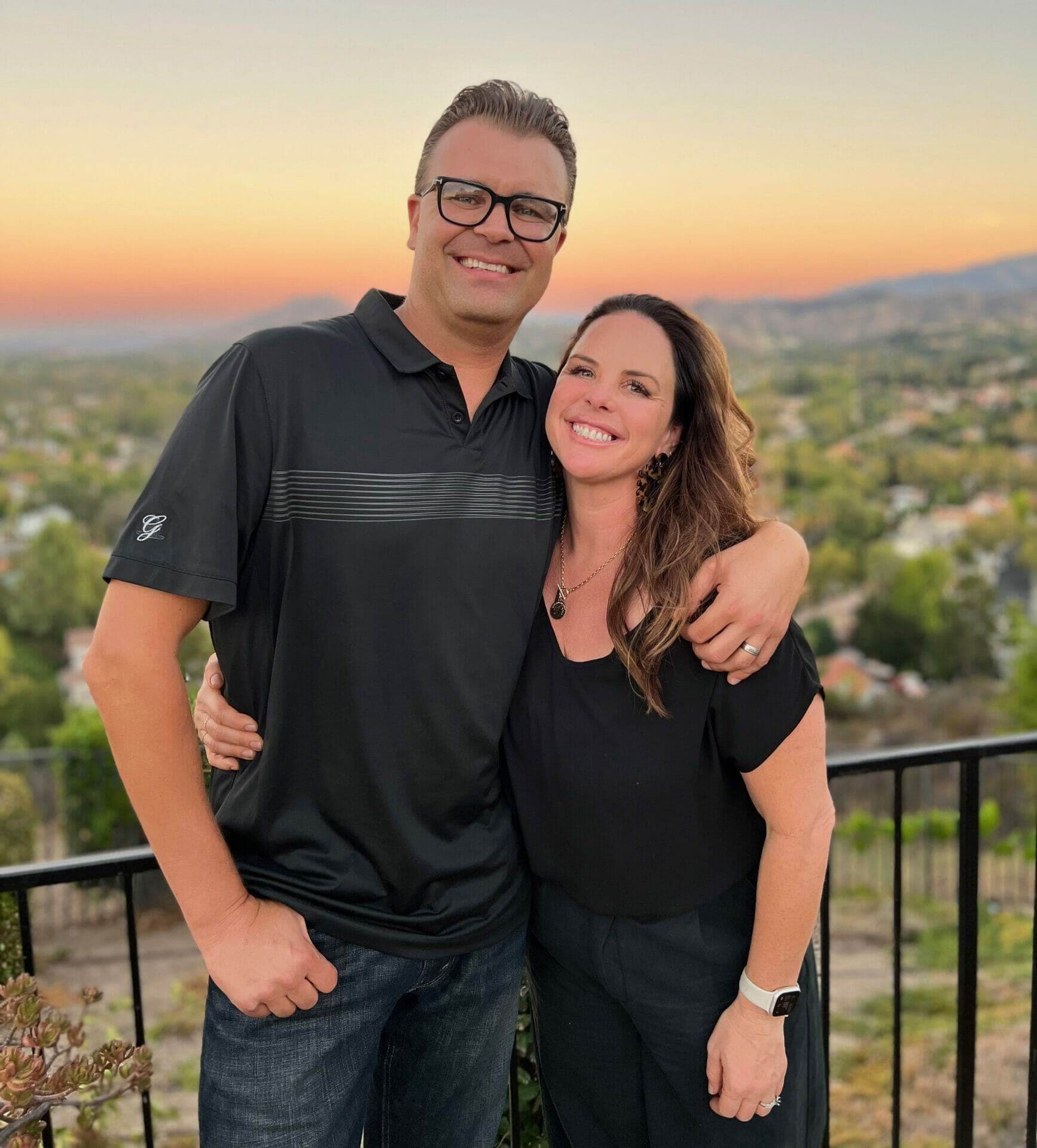 Michael and Cari smile together outdoors at sunset.