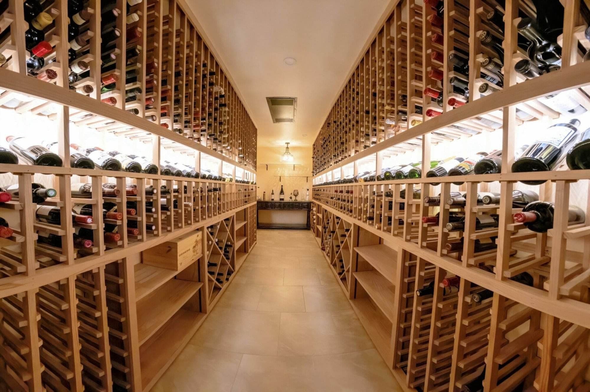 A bright cellar aisle runs between wooden racks with illuminated bottle display rows.