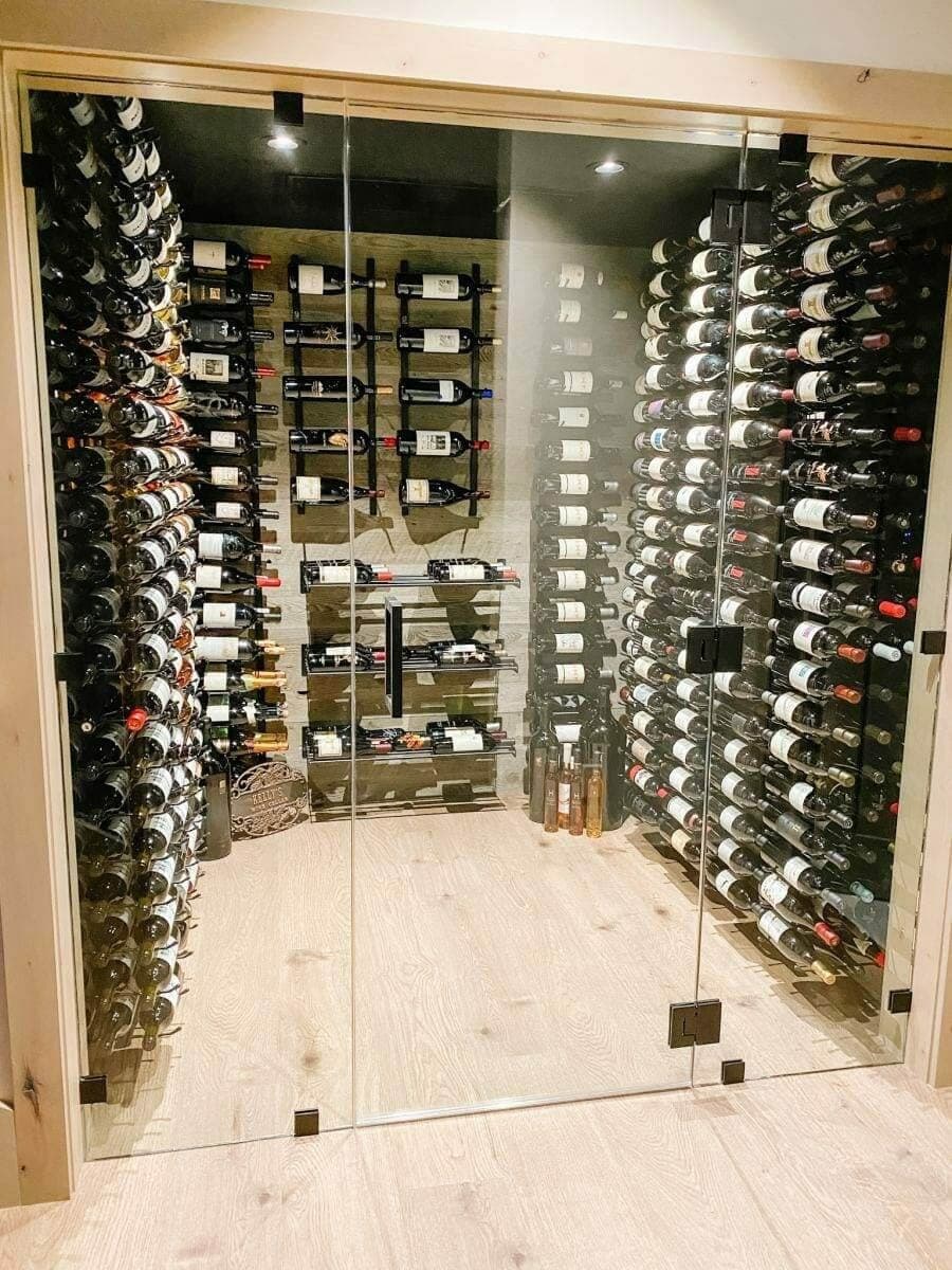Glass doors enclose a small cellar with metal bottle racks on three sides.