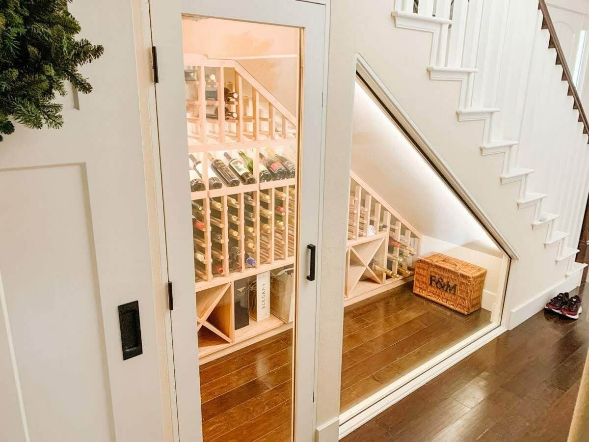 Glass doors reveal wooden wine racks beneath a staircase.