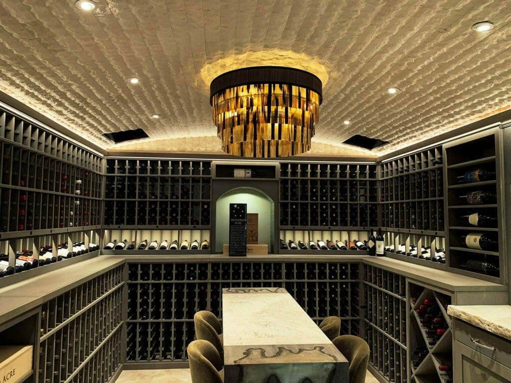 A tasting table sits inside a cellar lined with gray racks and illuminated bottle displays.