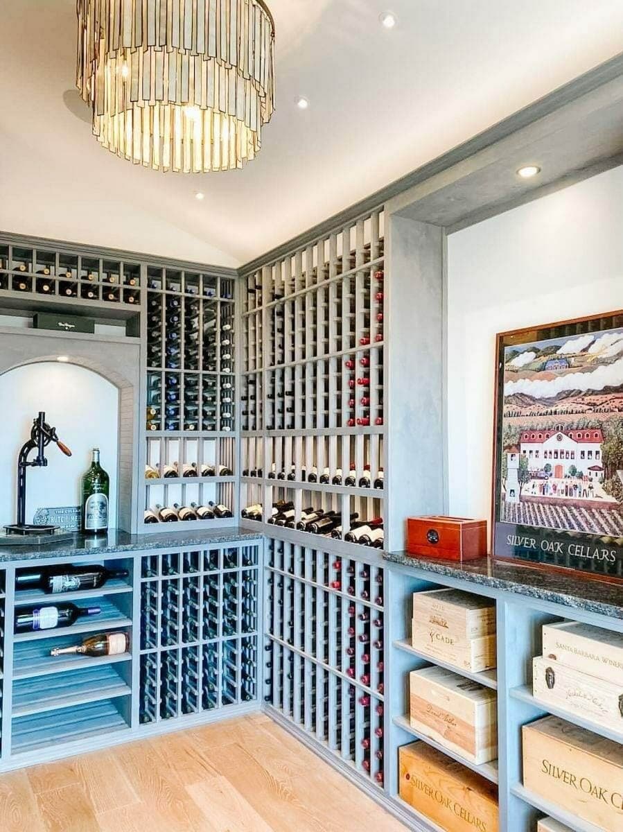 Gray cellar racks surround a display alcove and open shelves holding wooden wine cases.