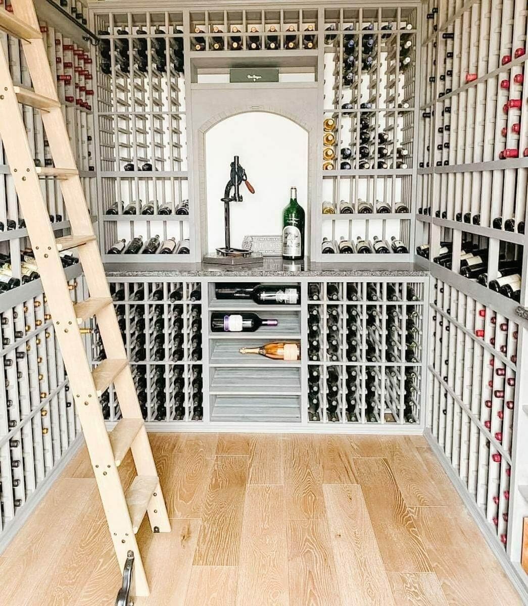 A wooden ladder stands beside gray bottle racks and an illuminated central display alcove.
