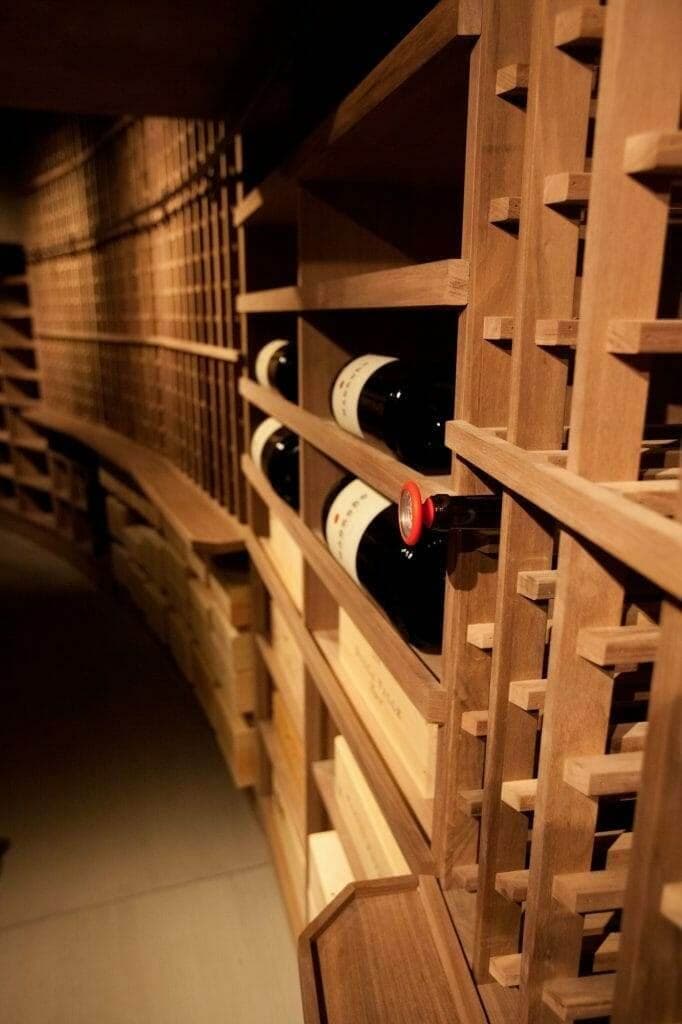 Curved wine cellar aisle with wooden diamond-bin racking and pendant bottles