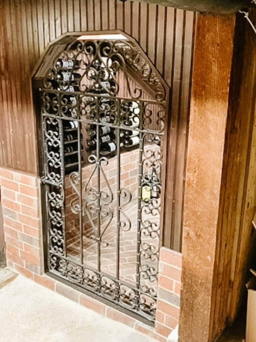Wrought-iron cellar gate framed by brick beside a wood-paneled wall