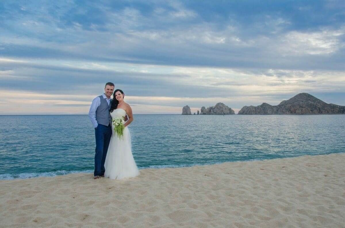 Couple posing together on a beach at dusk with rock formations offshore