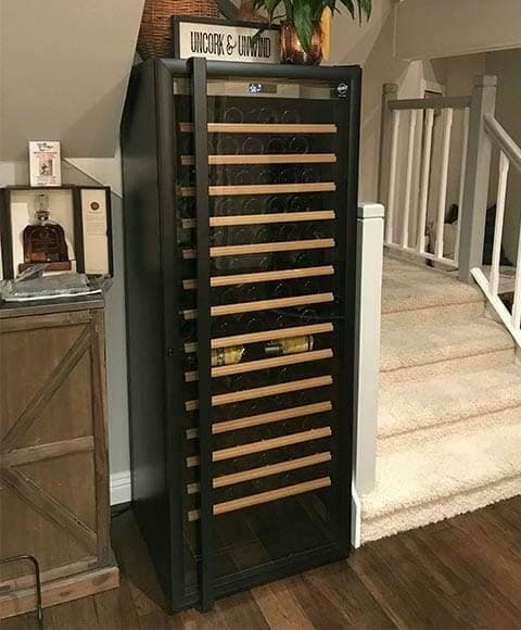 Black wine refrigerator with wood shelves installed beside a staircase