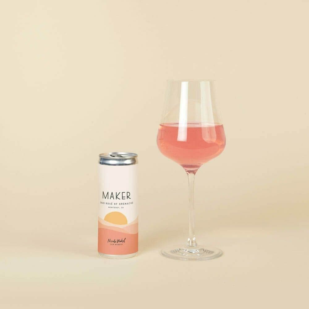 Maker Rose of Grenache can beside a filled wine glass on cream backdrop