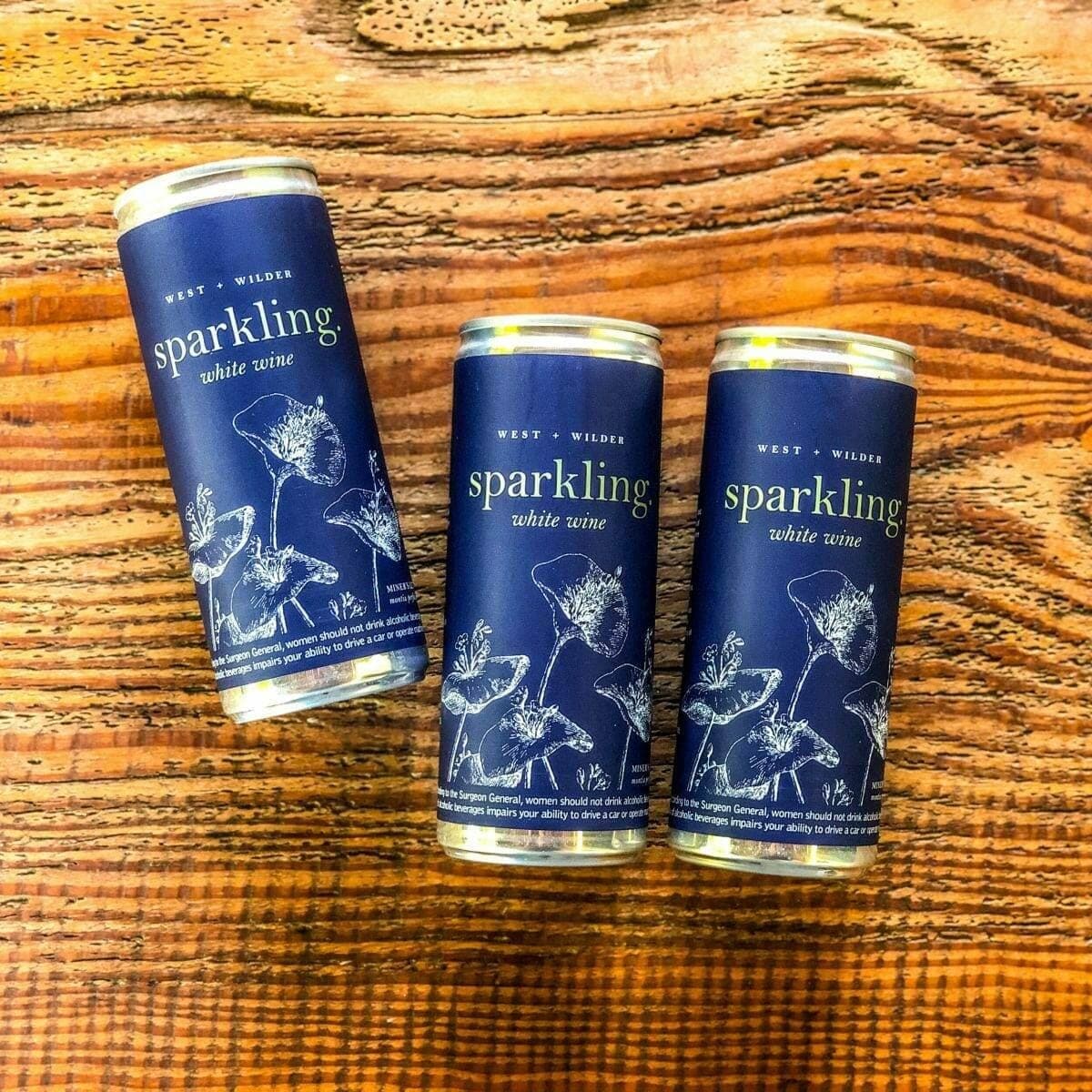 Three cans of West and Wilder sparkling white wine on rustic wood