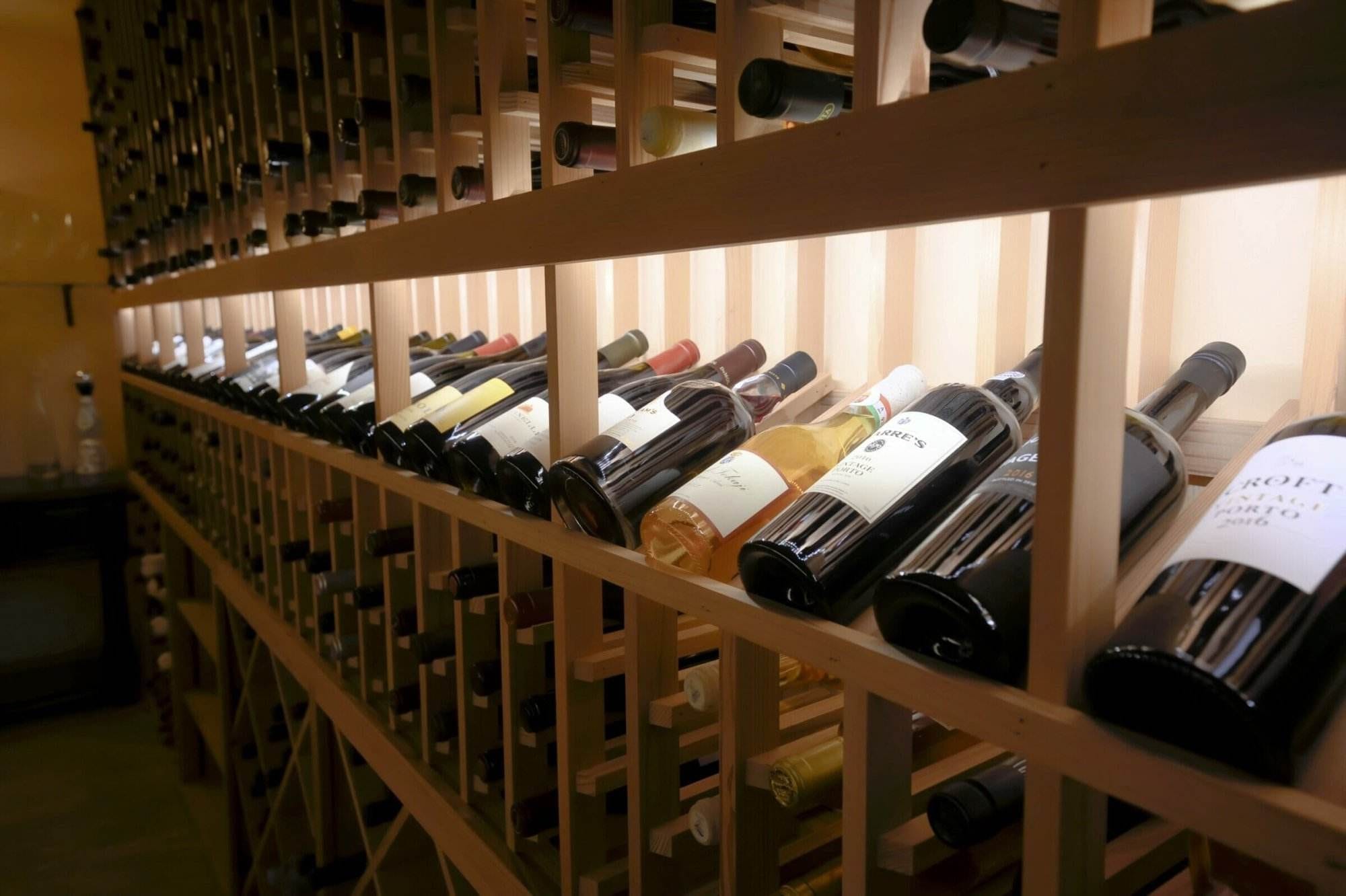 Wine bottles rest at an angle in an illuminated wooden display row.