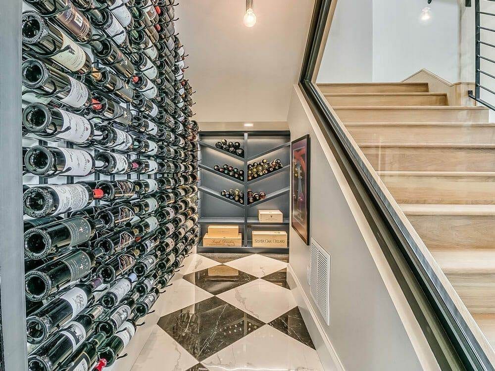 Angled glass wine wall filled with bottles beside a home staircase