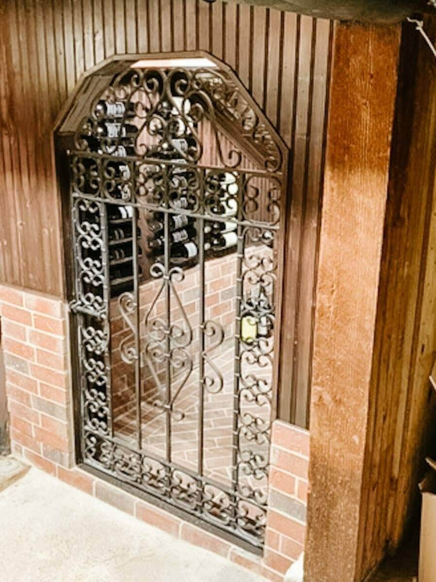 Wrought-iron cellar gate framed by brick beside a wood-paneled wall