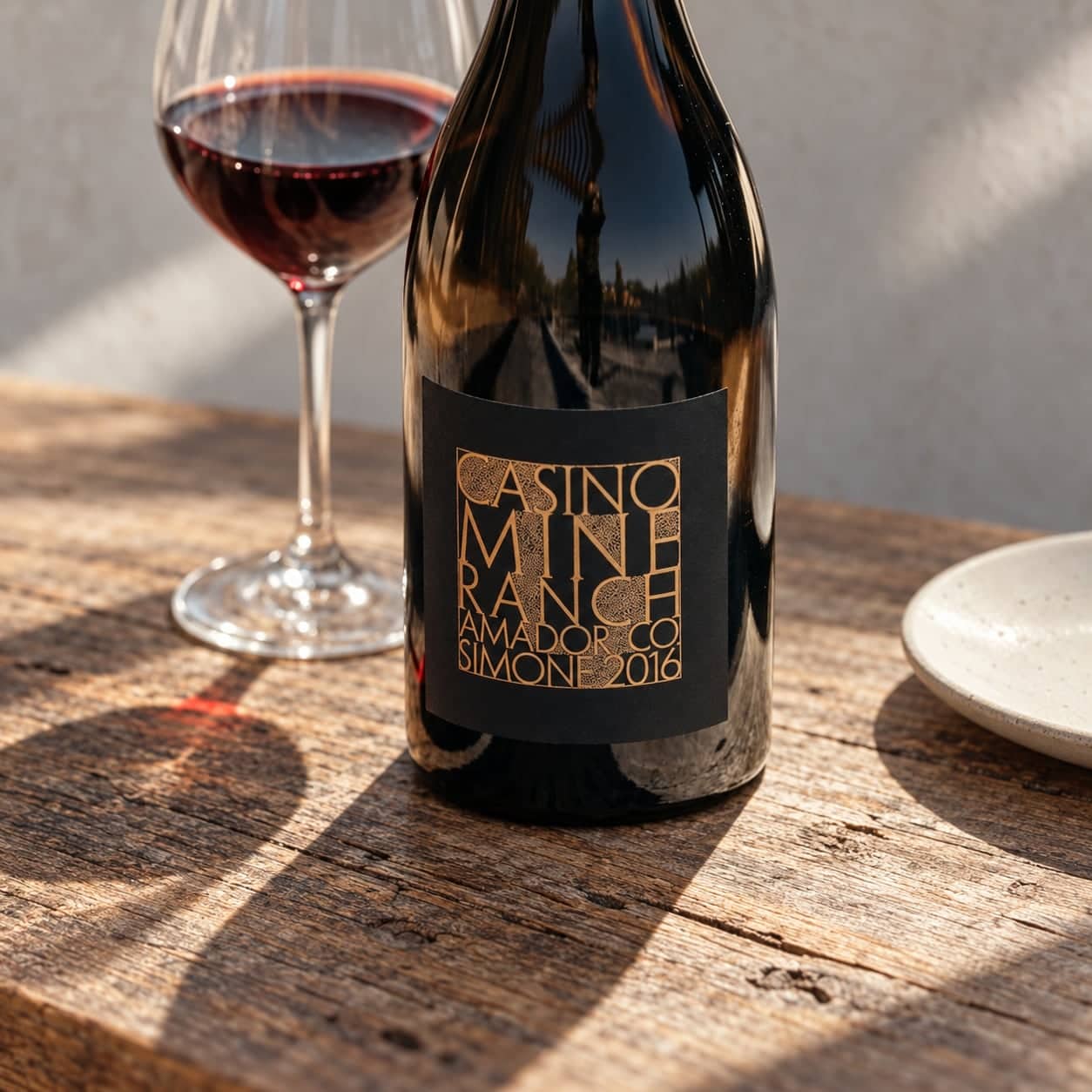 Casino Mine Ranch Simone 2016 bottle and wine glass on a rustic wood table with a plate