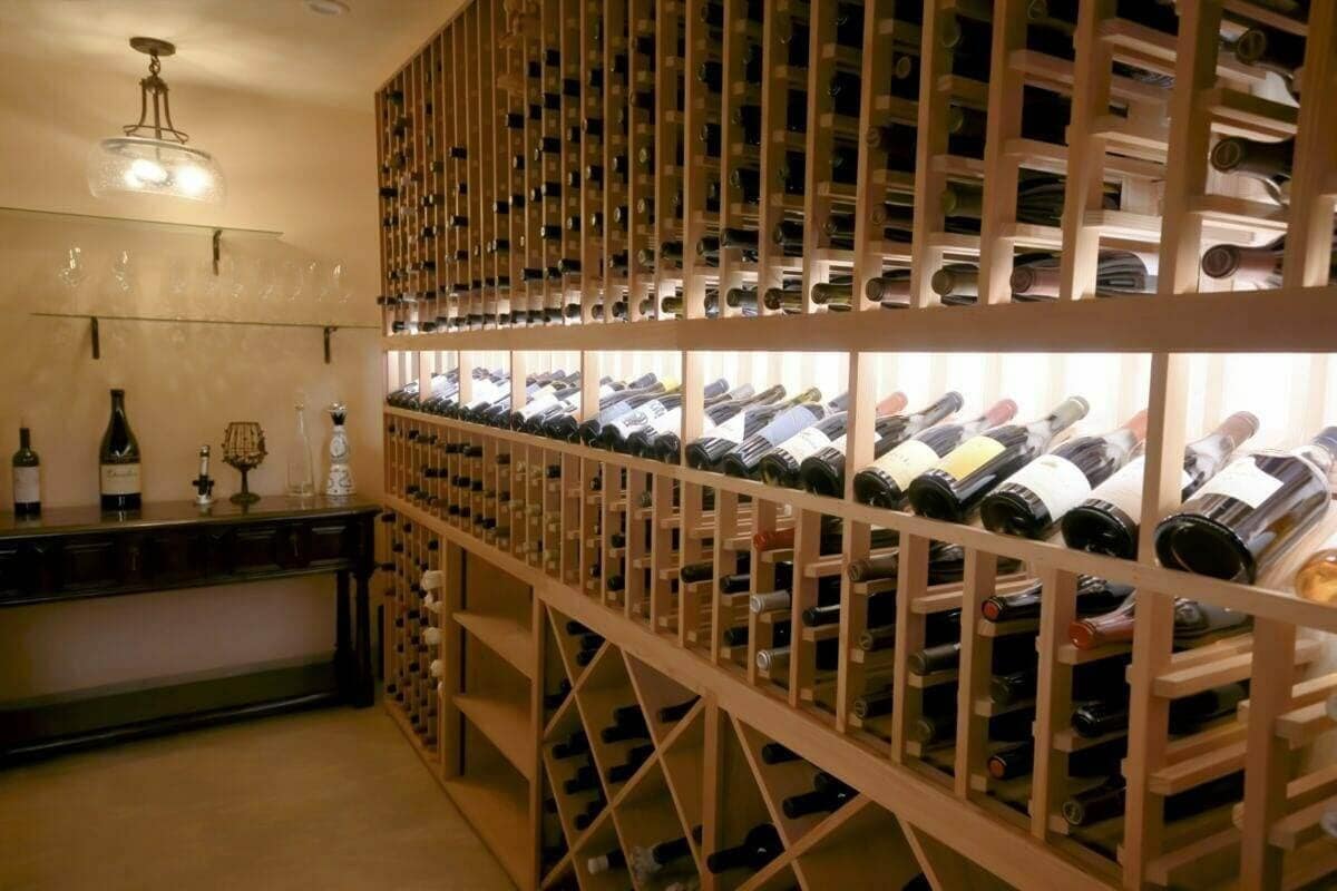 A long wooden rack wall with a lit display row stands beside a cellar bar.