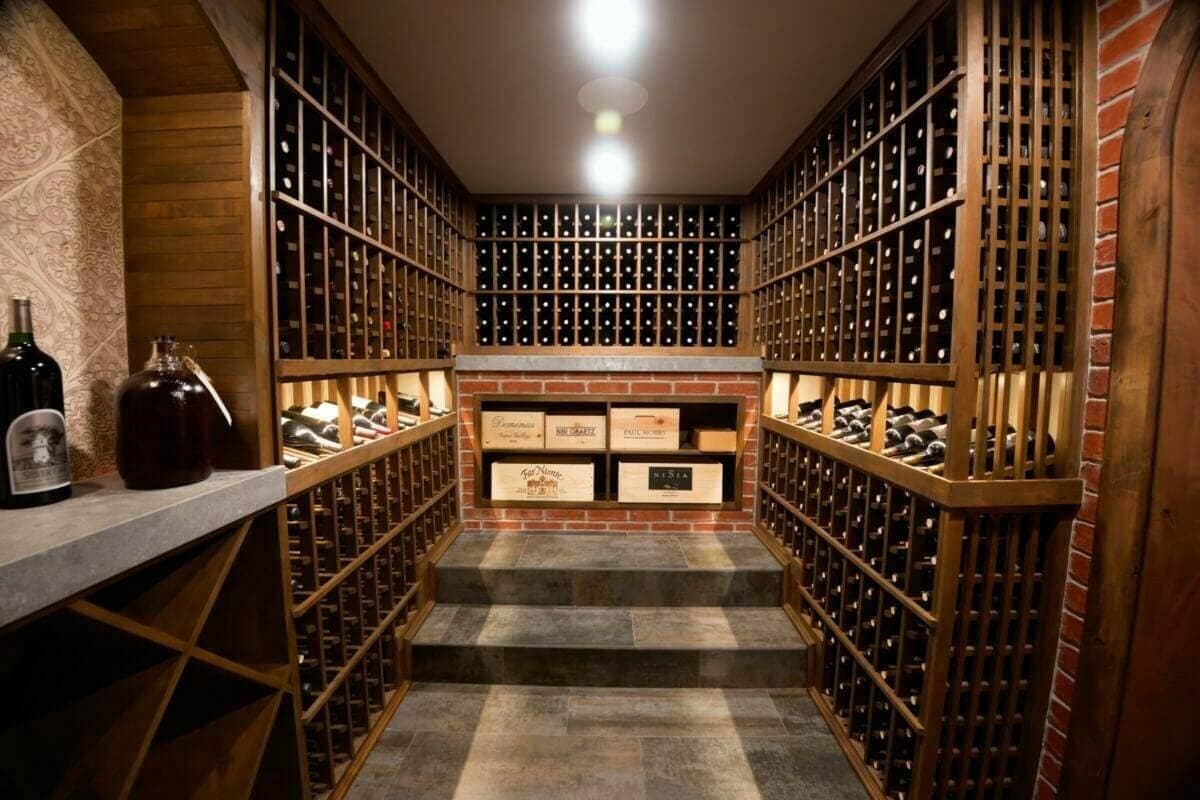 Wooden wine racks line a short cellar aisle leading to a raised storage alcove.