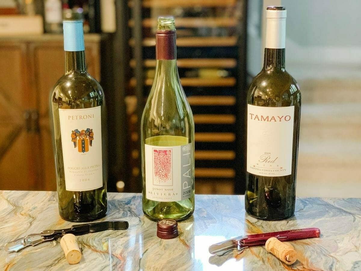 Three opened wine bottles, corks and corkscrews sit on a counter.
