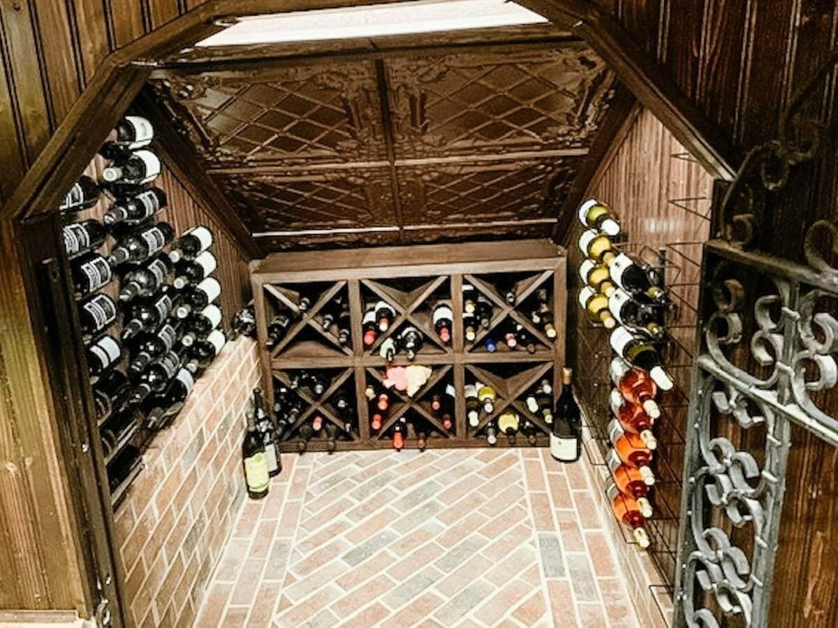 A small wood-paneled cellar has metal side racks, wooden diamond bins and a brick-pattern floor.