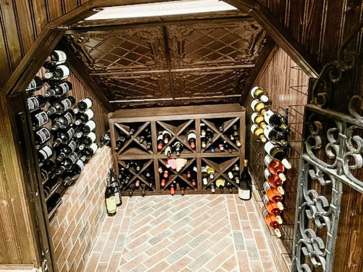 A small wood-paneled cellar has metal side racks, wooden diamond bins and a brick-pattern floor.