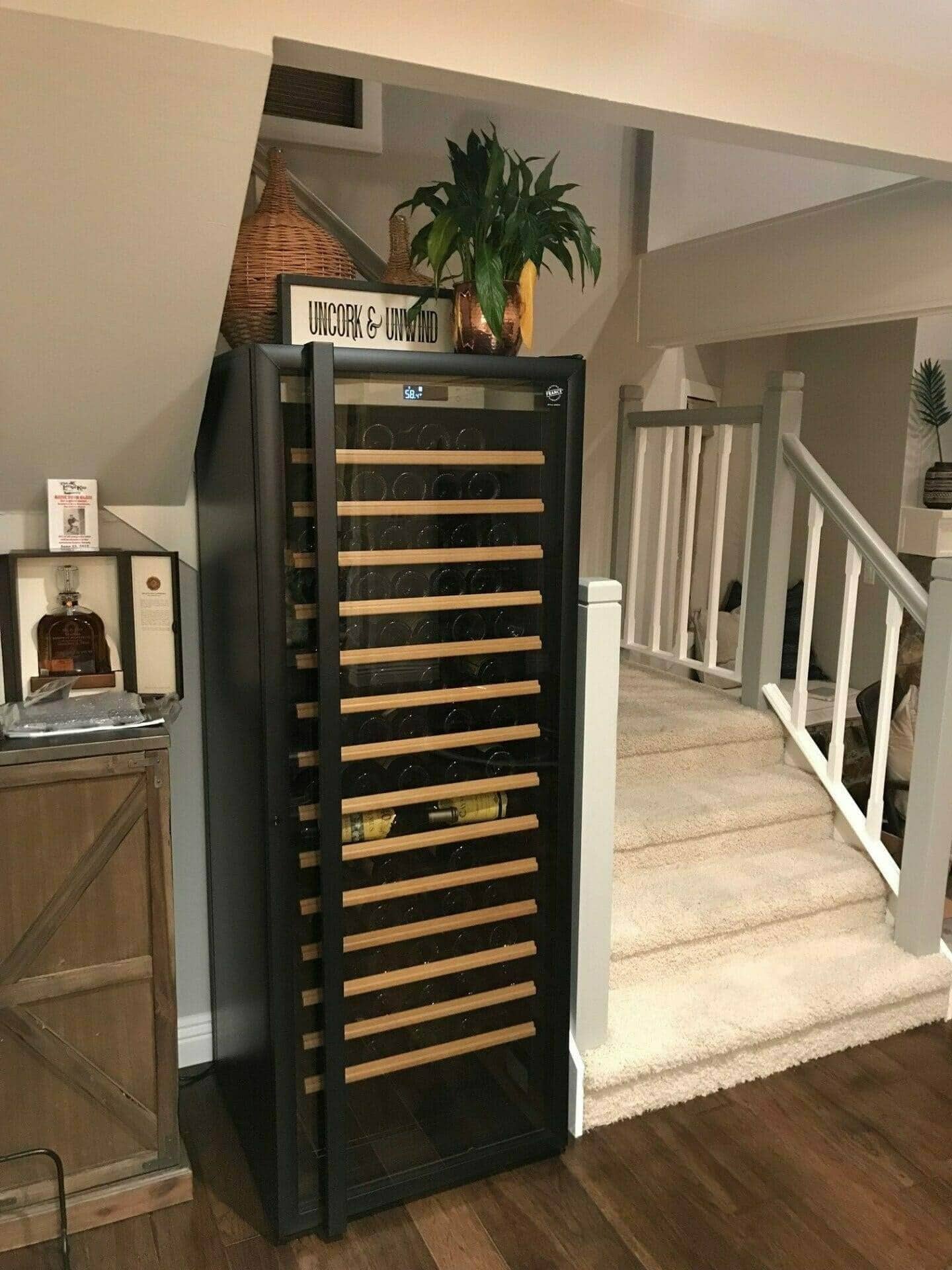 Freestanding wine cabinet in a home basement near a staircase and potted plant