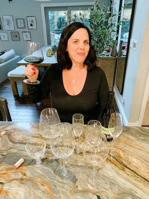 Woman holding a glass of red wine at a kitchen island with tasting glasses