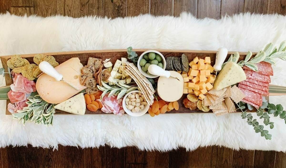 Long charcuterie board with meats, cheese and crackers on a white fur rug