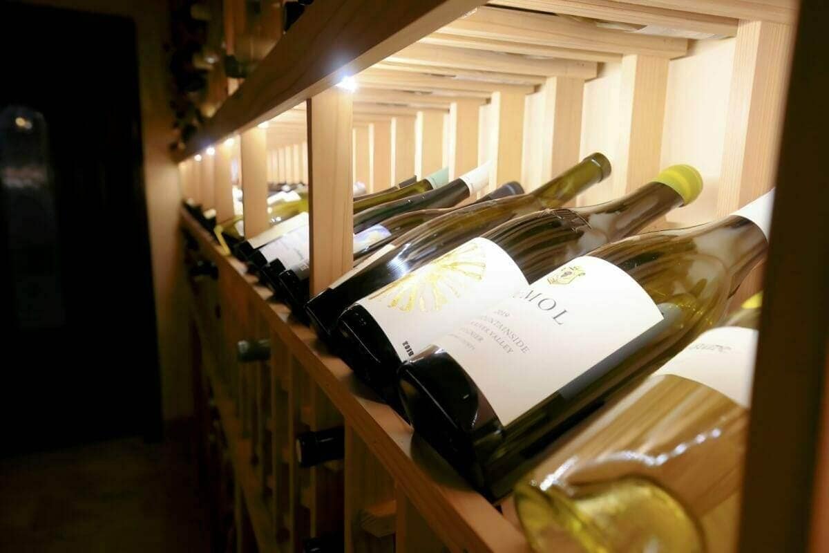 Close-up of white wine bottles resting on a lit wooden cellar rack.