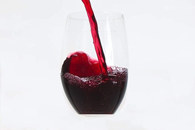 Red wine pouring into a stemless glass on white background