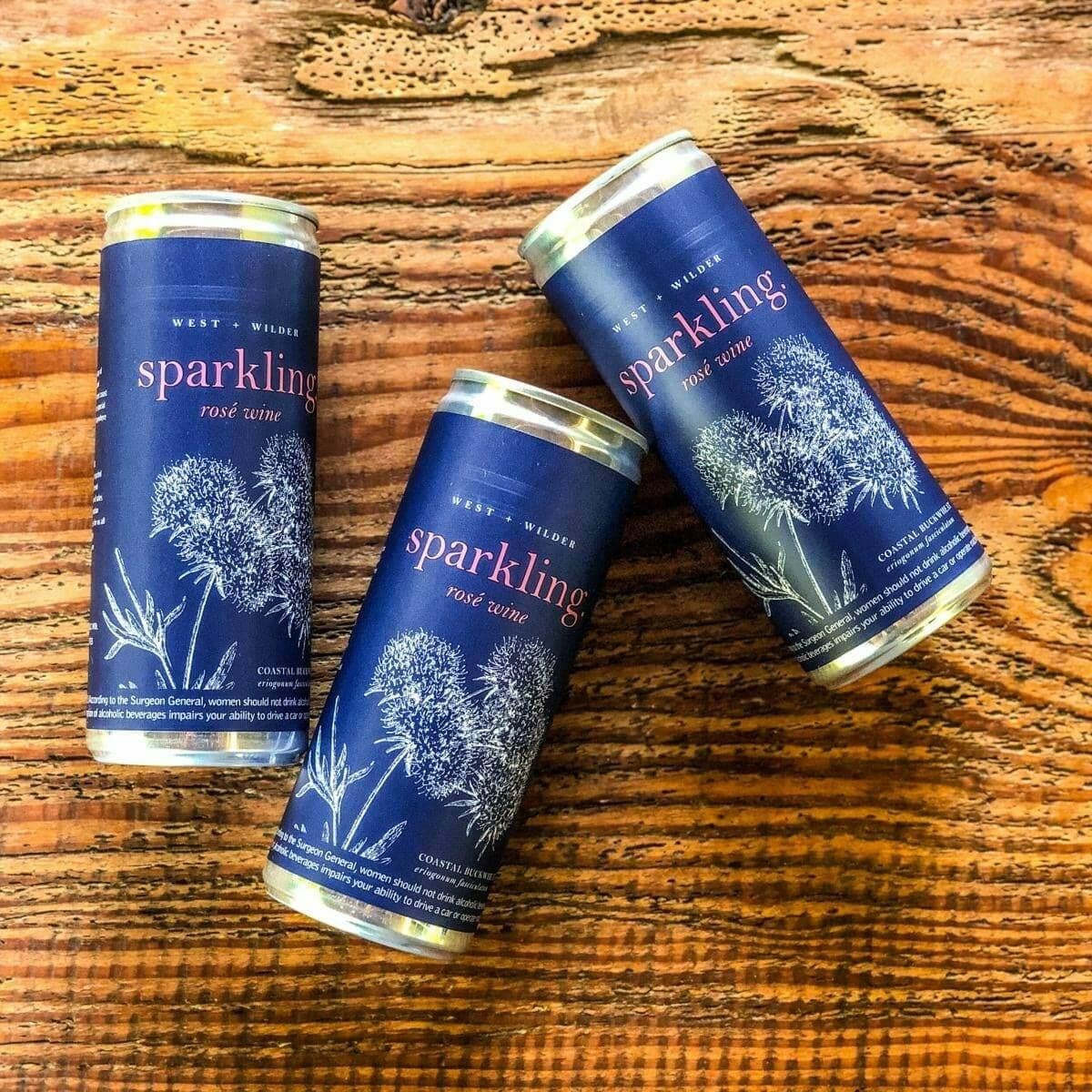 Three cans of West and Wilder sparkling rose wine on rustic wood