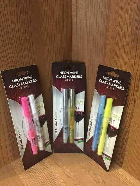 Three packs of neon wine glass marker pens on a wood shelf corner