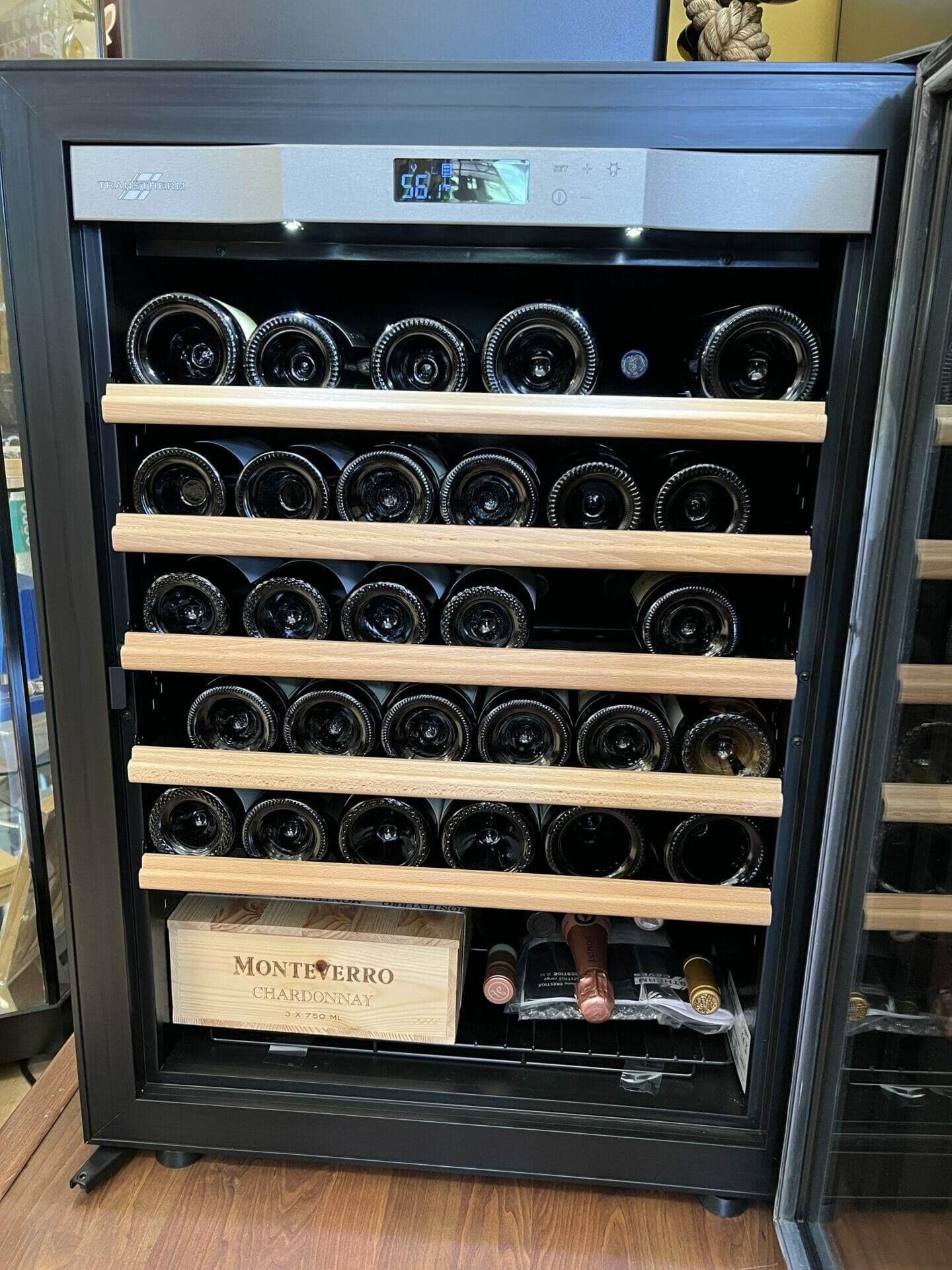 Transtherm wine cabinet interior, wood shelves of bottles above a Montiverro wine crate