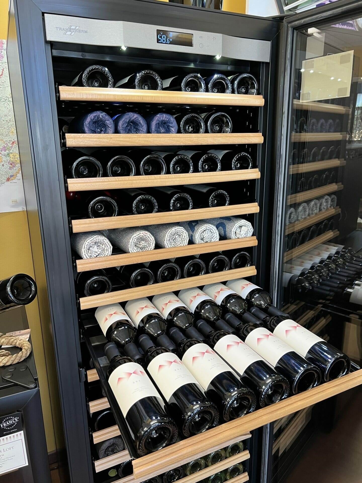 Transtherm wine cabinet drawer of red wine bottles beneath rolled towels and shelves