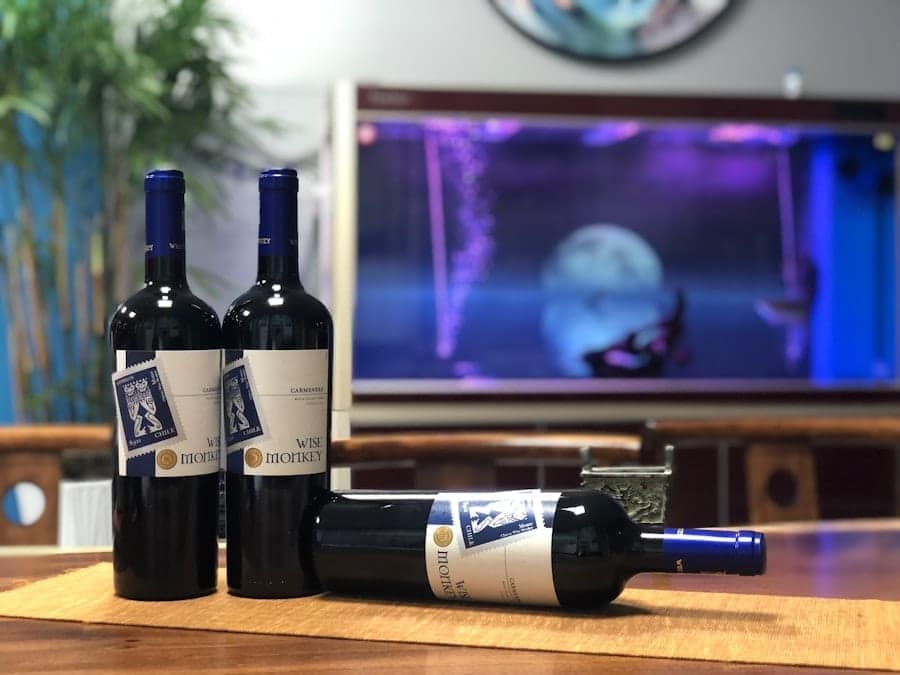 Three Wise Monkey wine bottles on a wood table with a TV behind